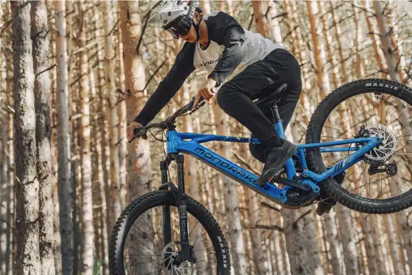 Biker in salto con la mountain bike in un bosco di pini