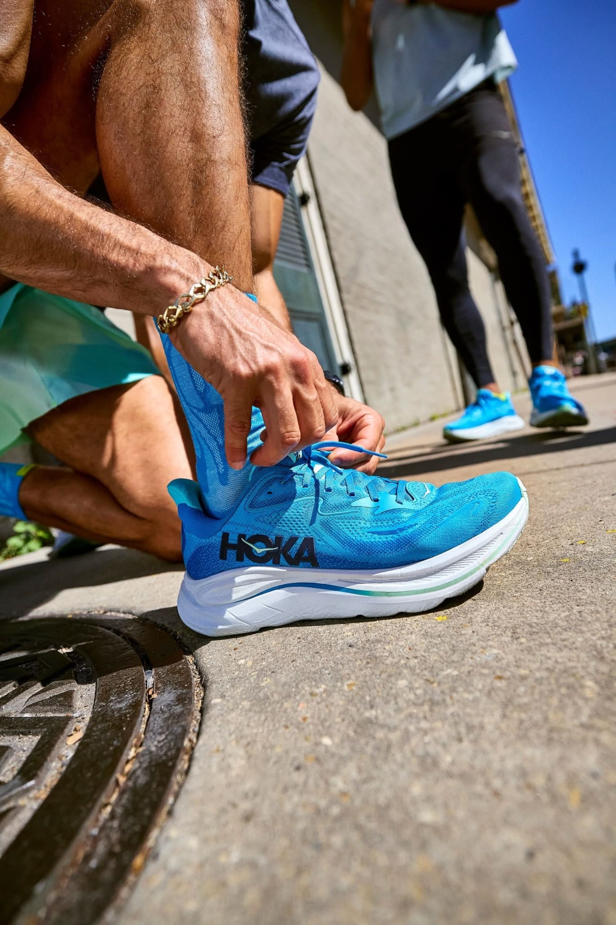 Runner che allaccia le scarpe da corsa azzurre sul bordo della strada